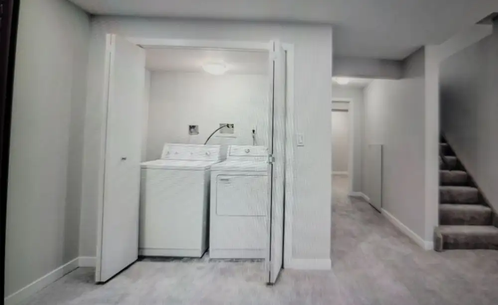 Finished basement hallway with a laundry closet with plumbing hookups and a carpeted staircase in a Calgary home