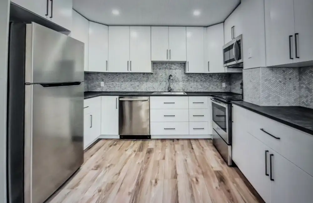 New kitchen with white cabinets, stainless appliances and vinyl plank flooring in a finished basement suite in Calgary