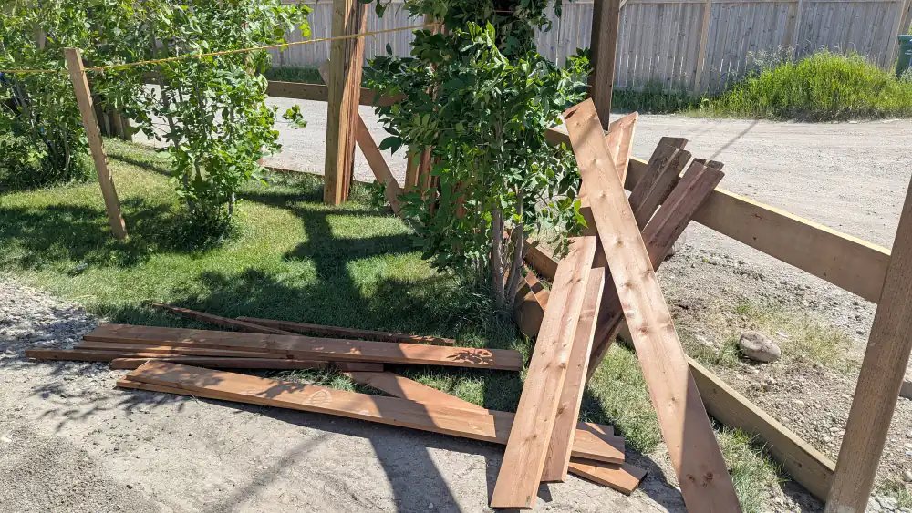 Broken wood fence boards and a collapsed frame lying on the ground beside a Calgary lane