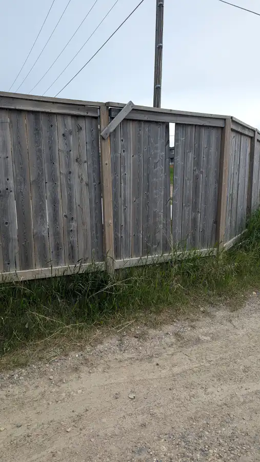 Wood fence with a broken top rail and leaning boards near a power pole beside a Calgary lane