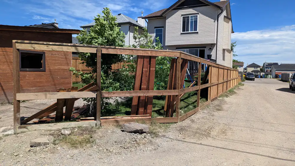 Collapsed wood fence section with exposed posts and rails along a back lane in Calgary before the rebuild