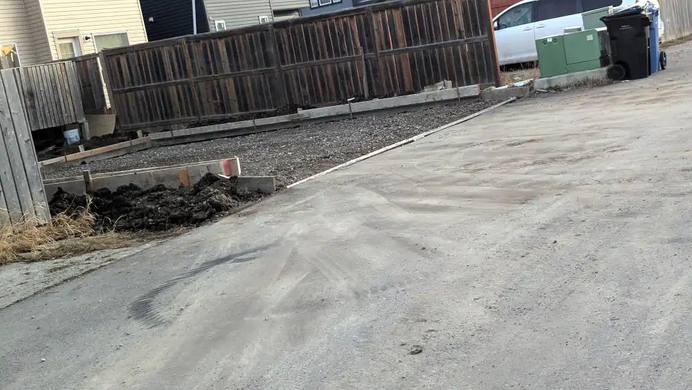 Compacted gravel base with wood forms set for a concrete pad on a Calgary back lane