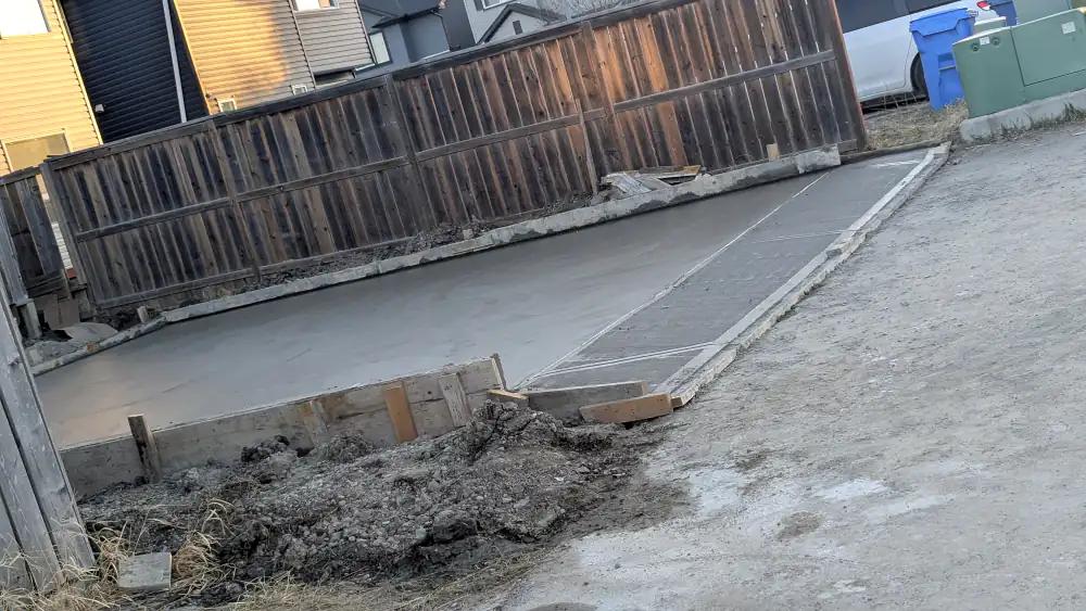 Edge of a new concrete pad with wood forms and a sloped transition to the lane in Calgary