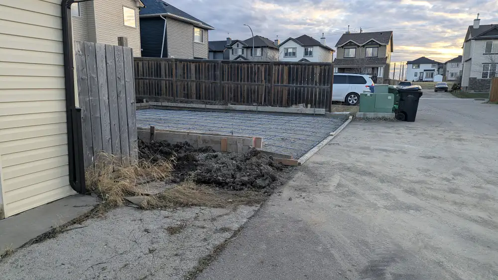 Wood forms and compacted gravel prepared for a new concrete pad beside a fence on a Calgary back lane