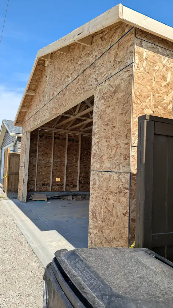 Detached garage with framed walls, OSB sheathing, gable trusses and an open door bay on a Calgary back lane