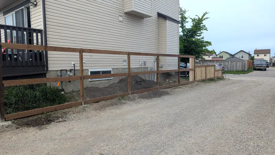 Wood fence frame with posts and rails along a back lane beside a house in Calgary before boards were attached