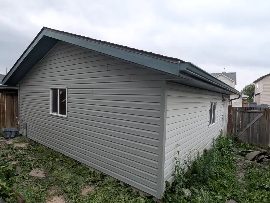 Side wall of a Calgary house covered with new vinyl siding, corner trim and soffit after installation