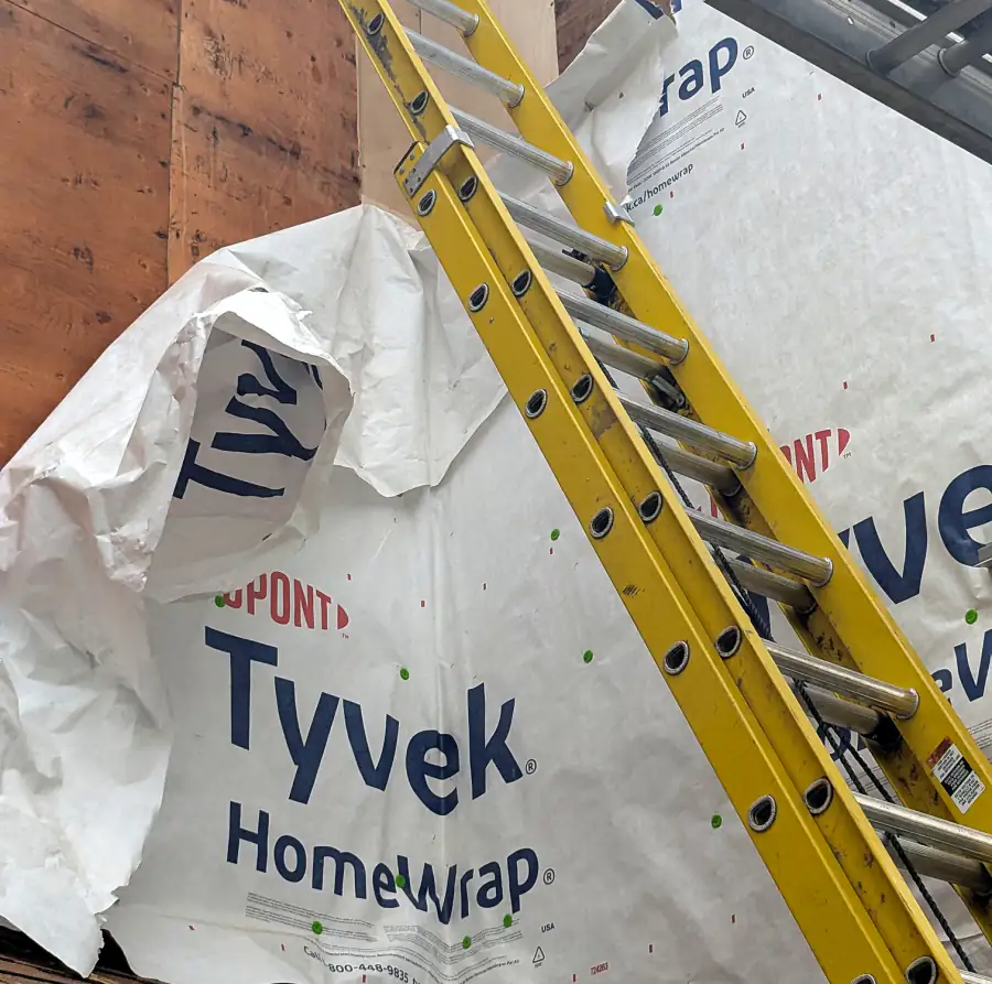 Tyvek house wrap on a Calgary home wall with a ladder, ready for new siding