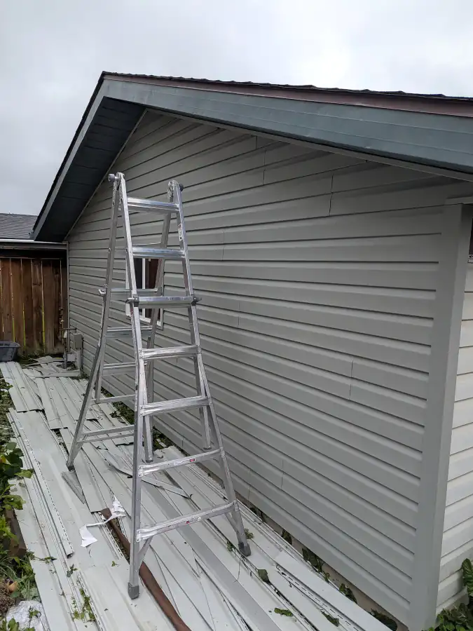 New vinyl siding panels installed on a side wall of a Calgary house with a ladder and leftover old siding on the ground