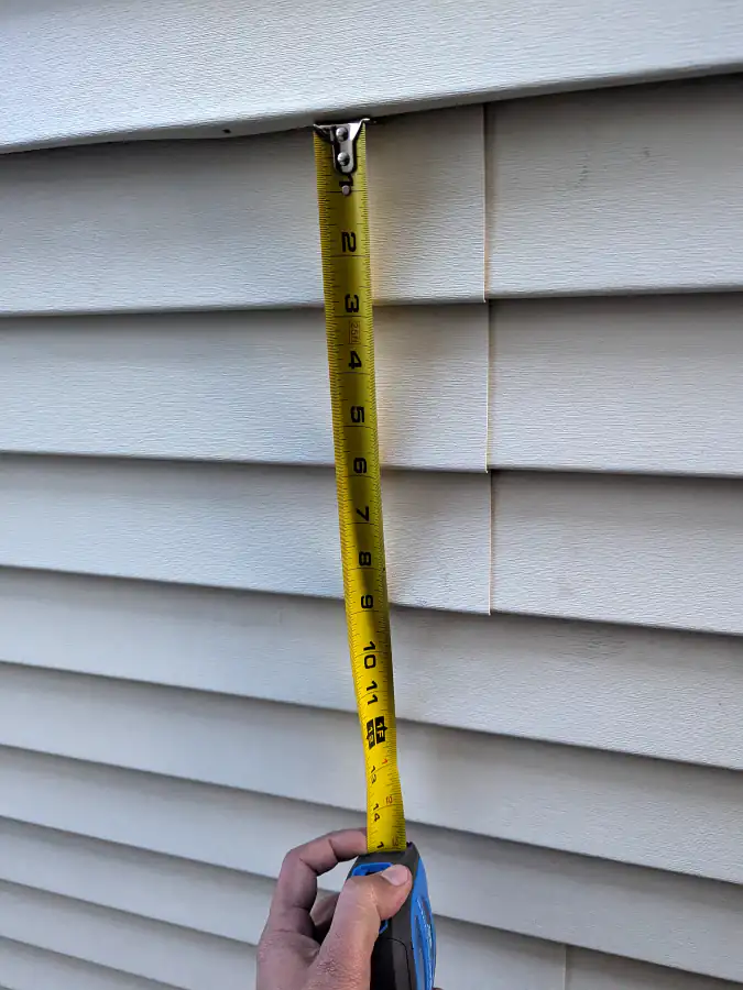 Tape measure held against vinyl siding panels during a hail damage inspection in Calgary