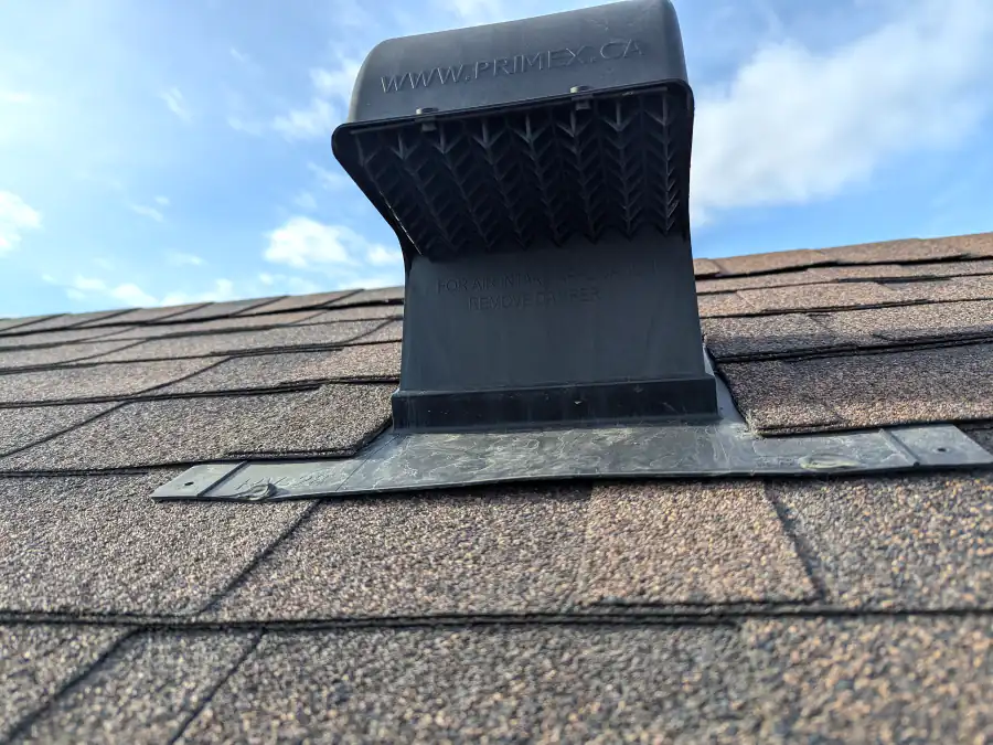 Close up of a black roof vent with a metal flashing flange on an asphalt shingle roof in Calgary