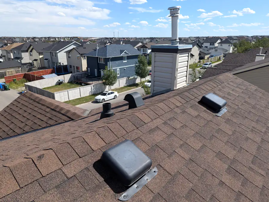 Roof vents and a chimney on an asphalt shingle roof in Calgary, common leak points checked in a roof repair