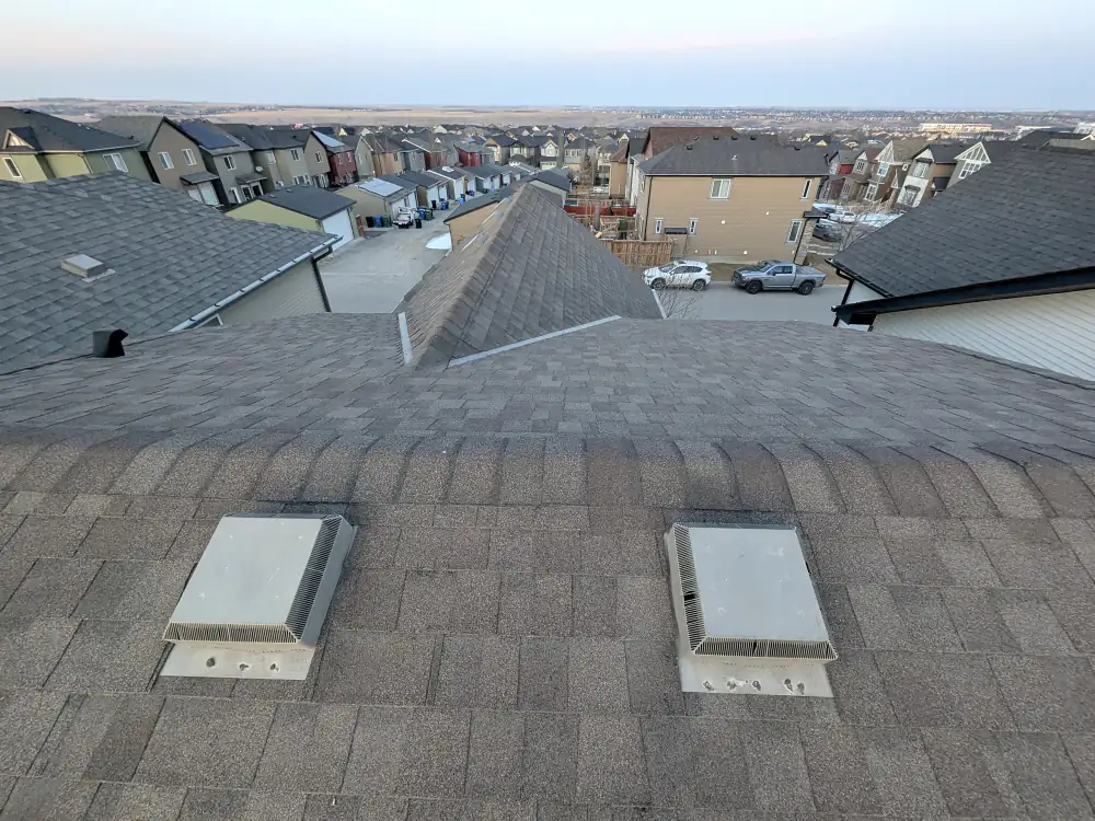 Asphalt shingle roof with two roof vents seen from the ridge on a Calgary house at dusk