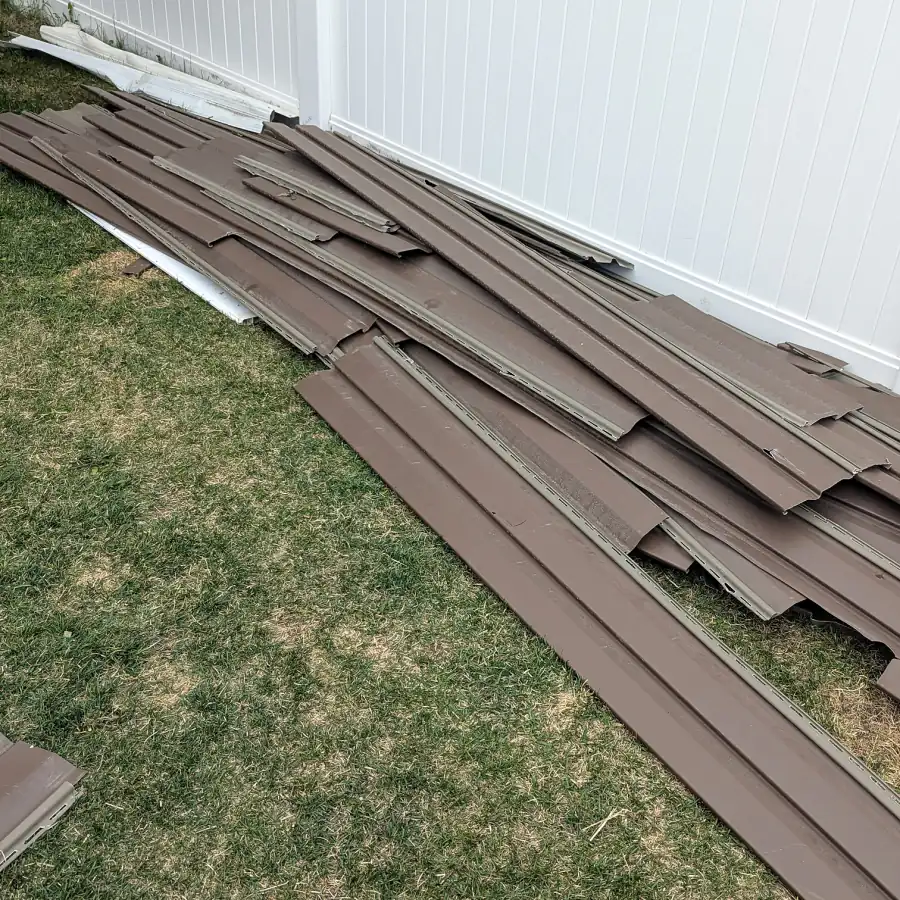 Siding panels stacked on a lawn beside a white fence after a siding job in Calgary