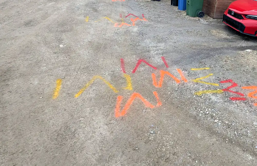 Utility locate paint marks on a gravel lane in Calgary, marked before digging for a fence and concrete job