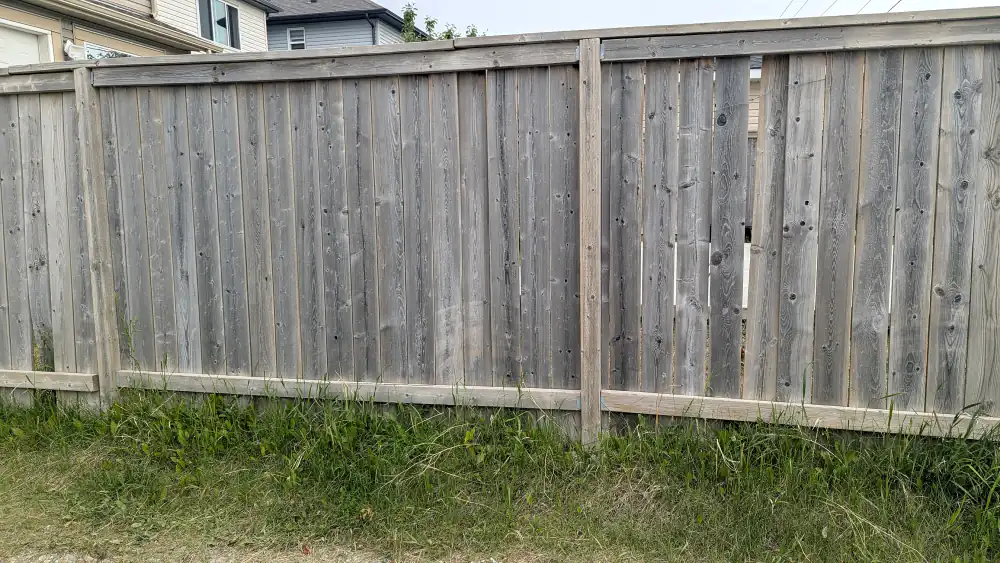 Weathered grey wood fence with loose boards and gaps between boards along a Calgary lane before repair